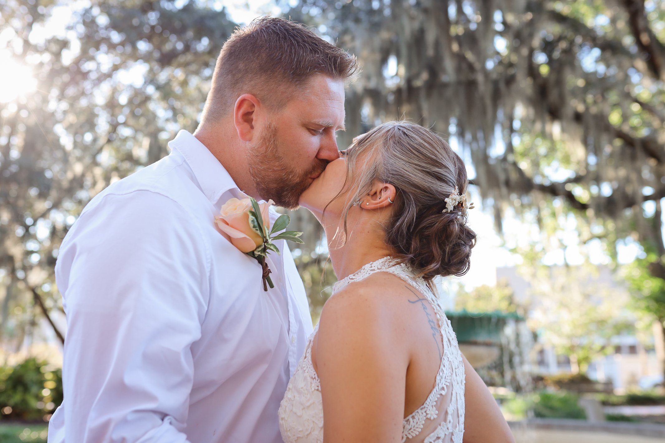 A newlywed couple sharing a kiss beneath Savannah's trees